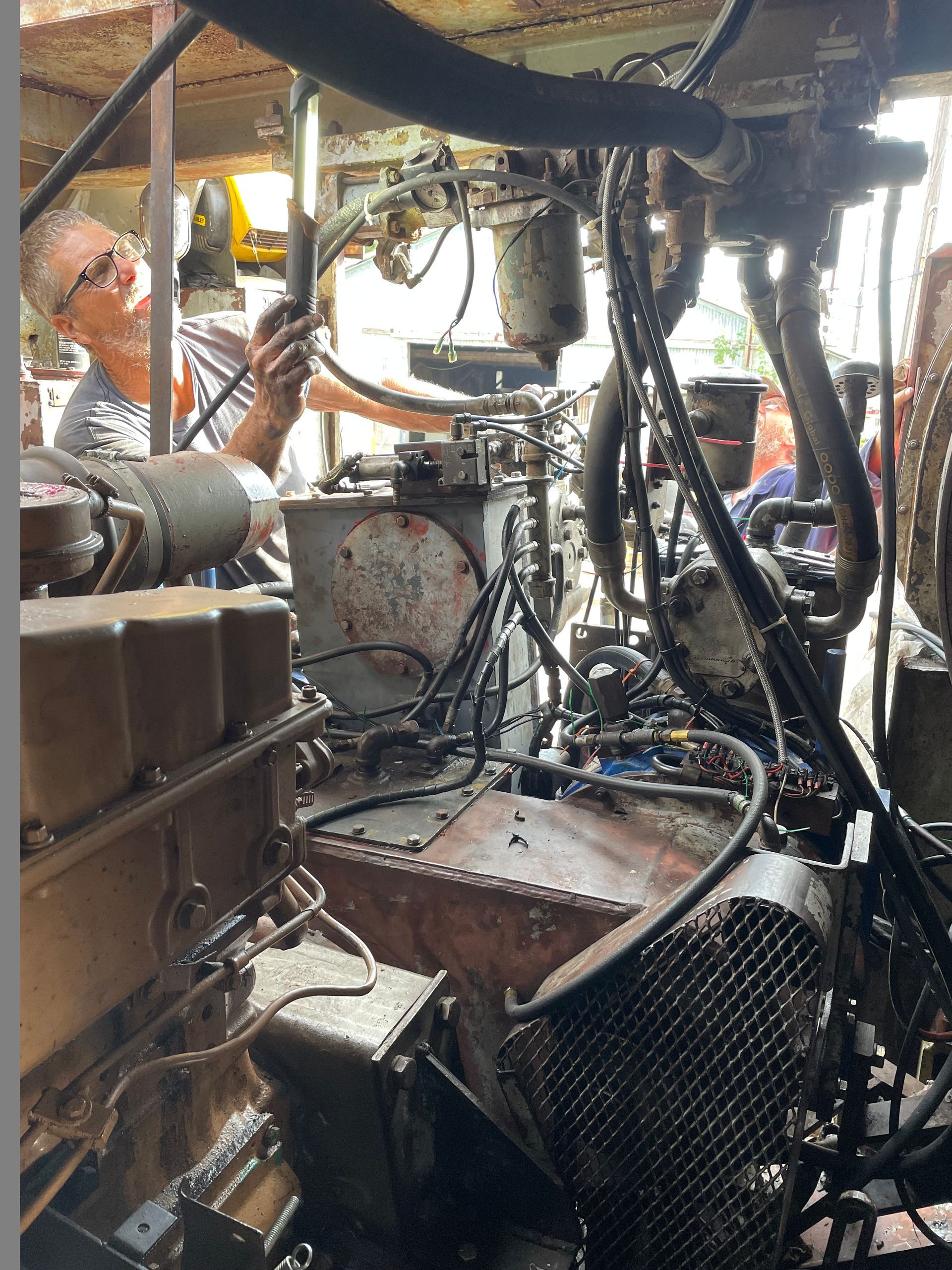Man inspecting machinery, possibly an engine, inside a cluttered, industrial-looking space.