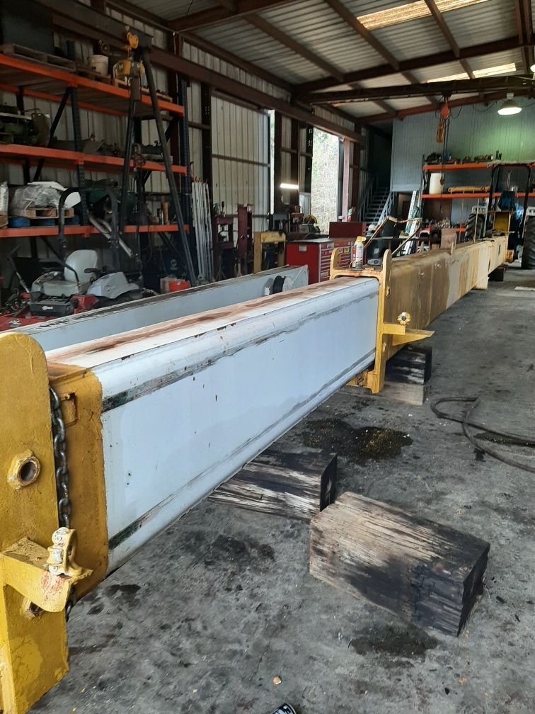 A long, yellow and white industrial beam inside a workshop, supported by wooden blocks.