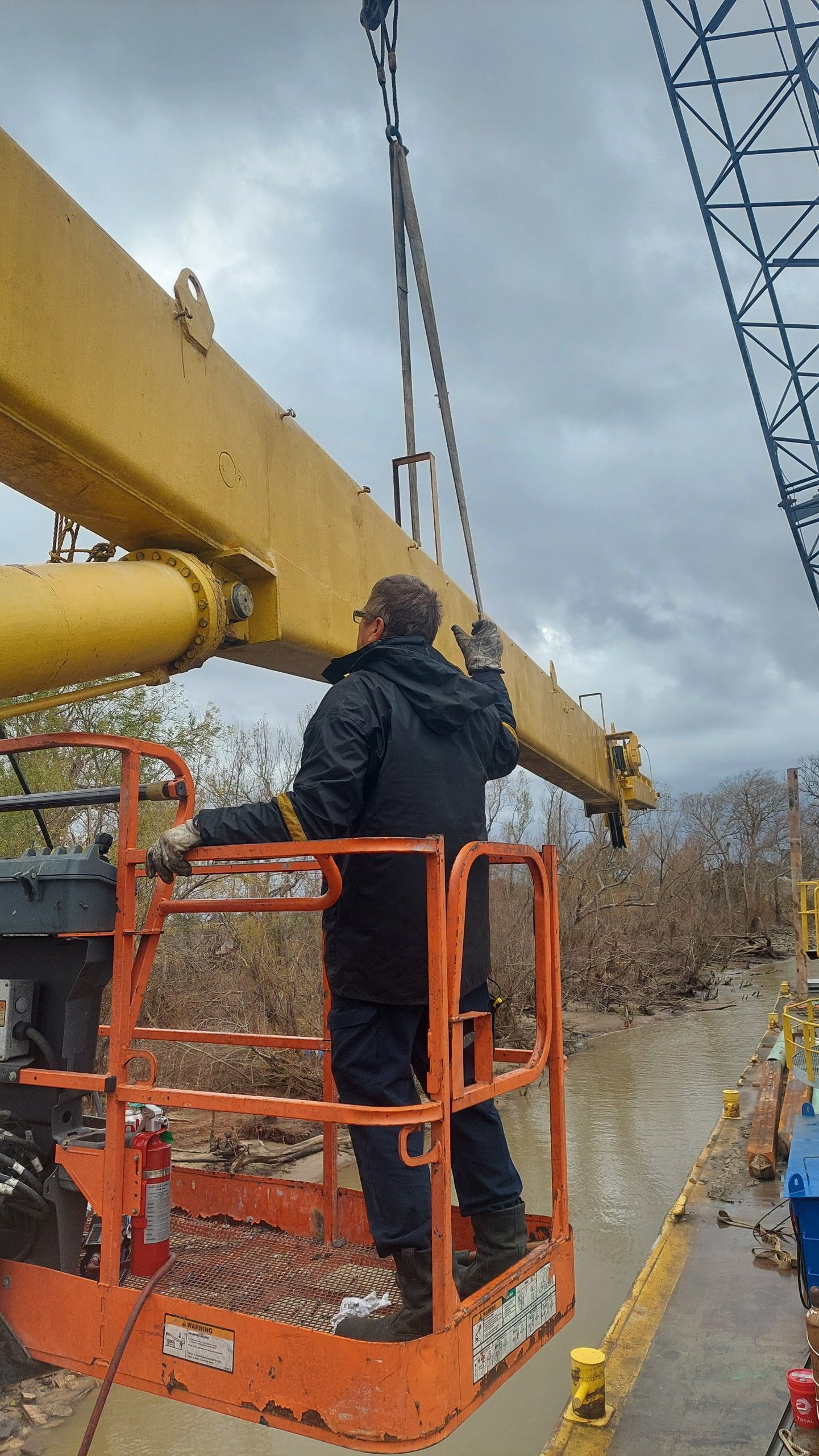 Worker in lift adjusts yellow crane arm, with cloudy sky.