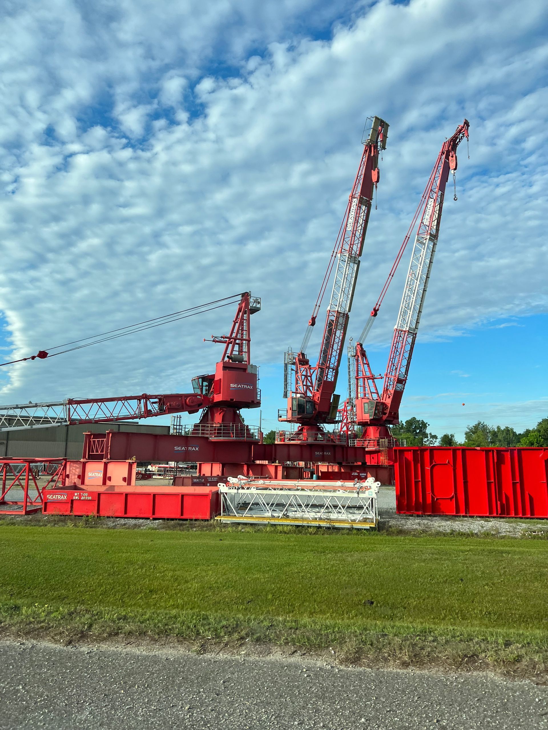 Three large red cranes on a barge against a cloudy sky.