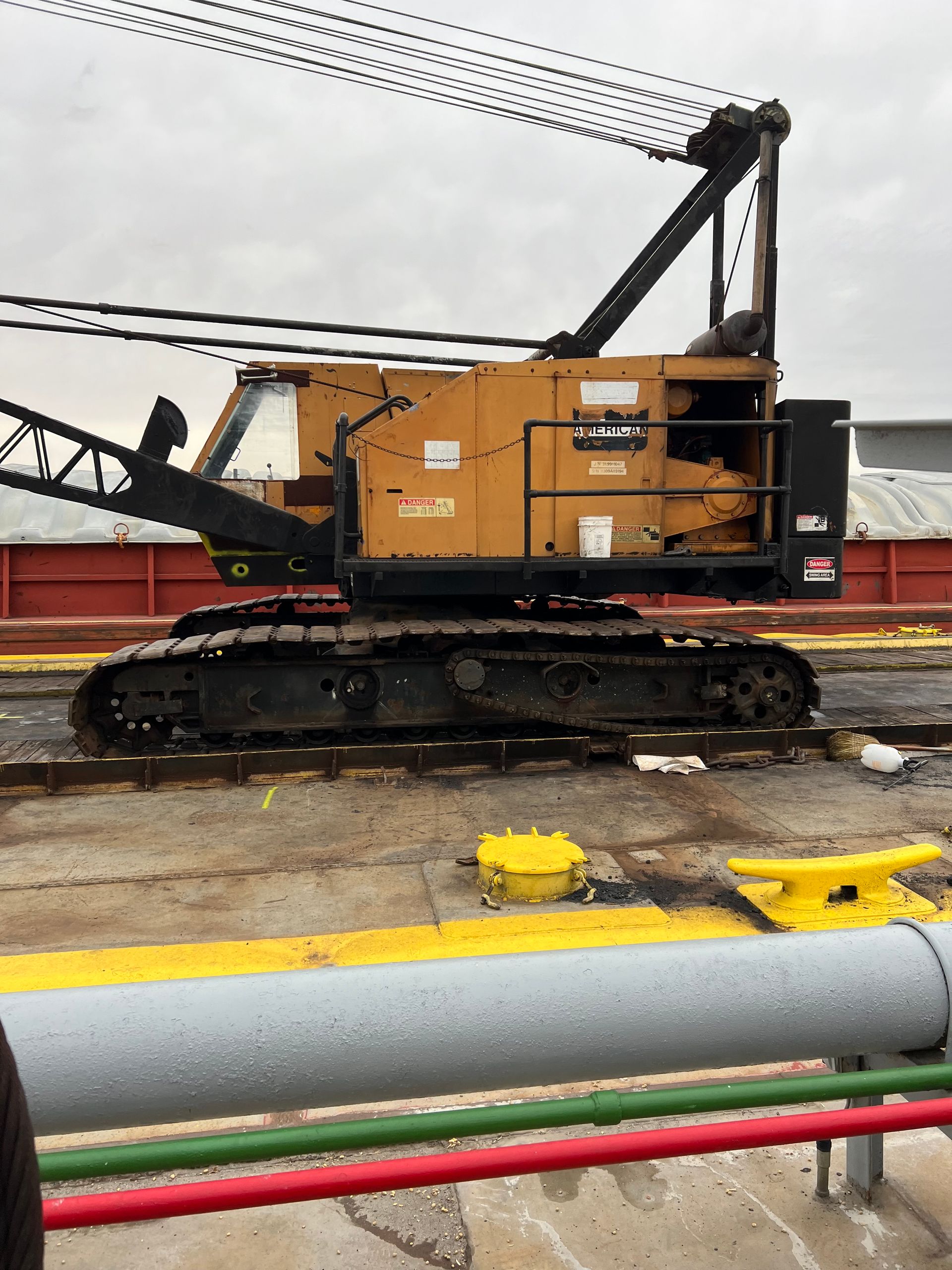 Yellow crawler crane on a dock, black tracks, against a cloudy sky.