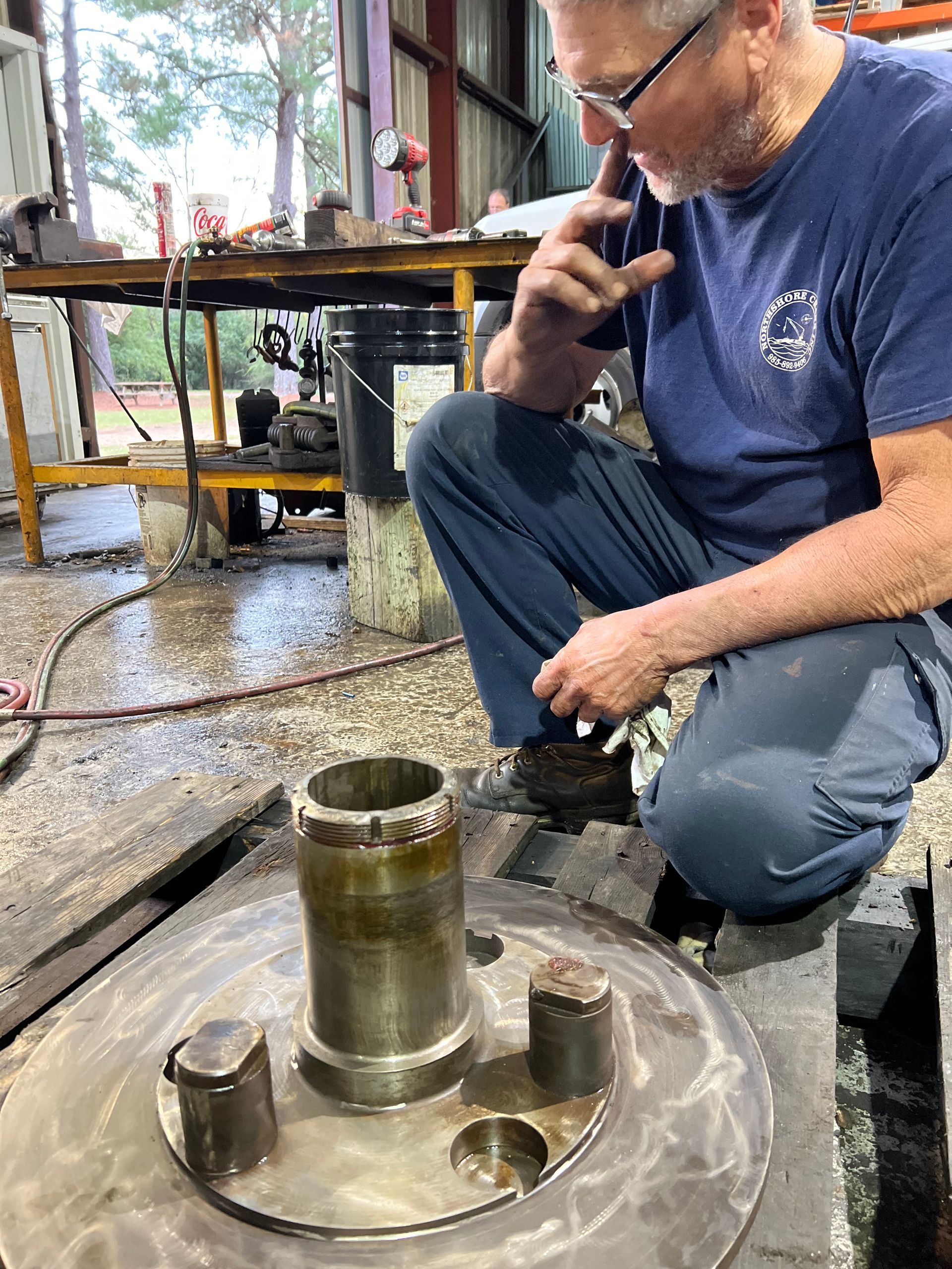 Man inspecting machinery component, crouching in workshop.