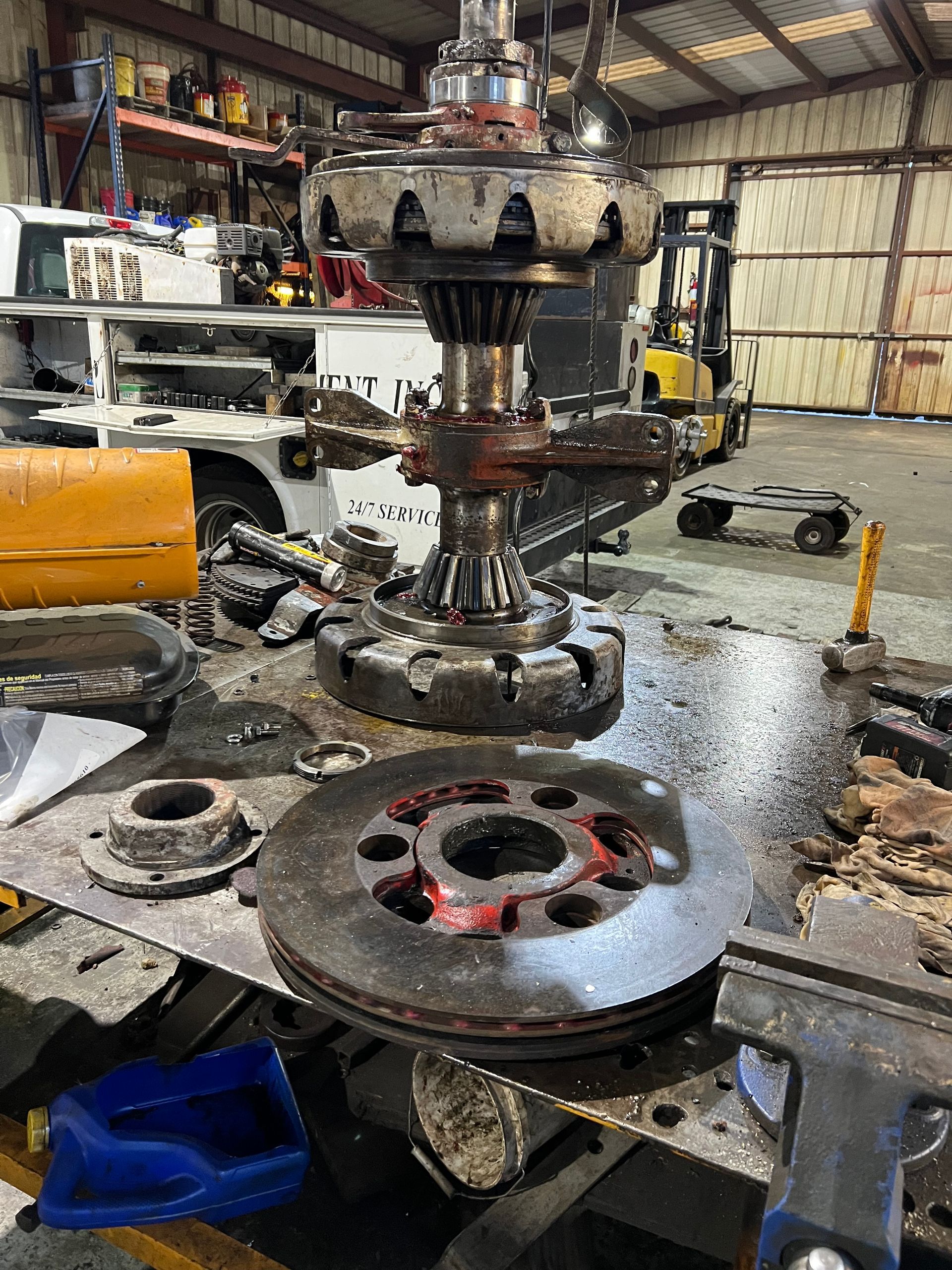 Machinery repair. Metal parts on a workbench inside a workshop, including gears, a brake rotor, and a large central mechanism.