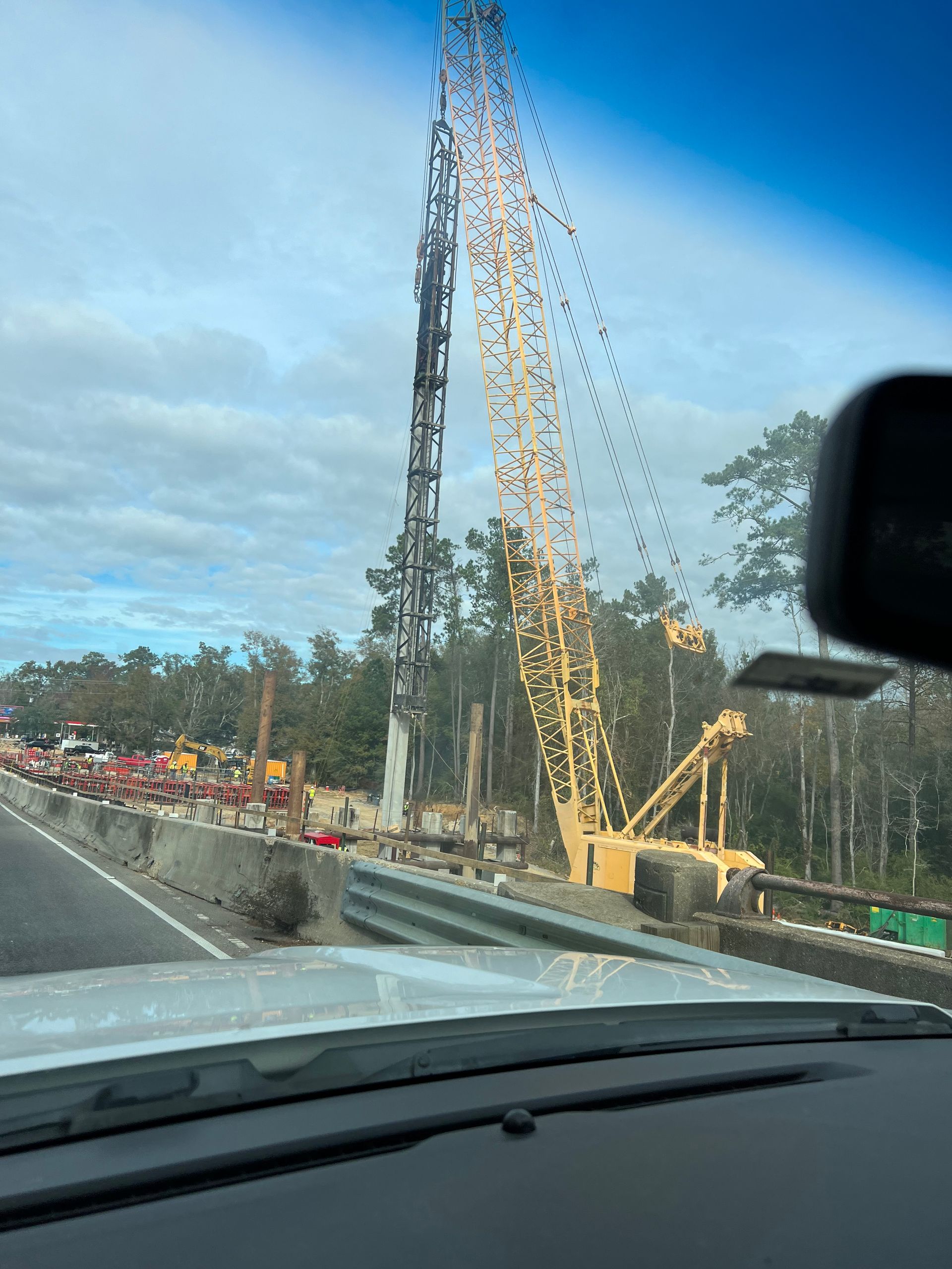 Construction site with crane, highway barrier, and cloudy sky.