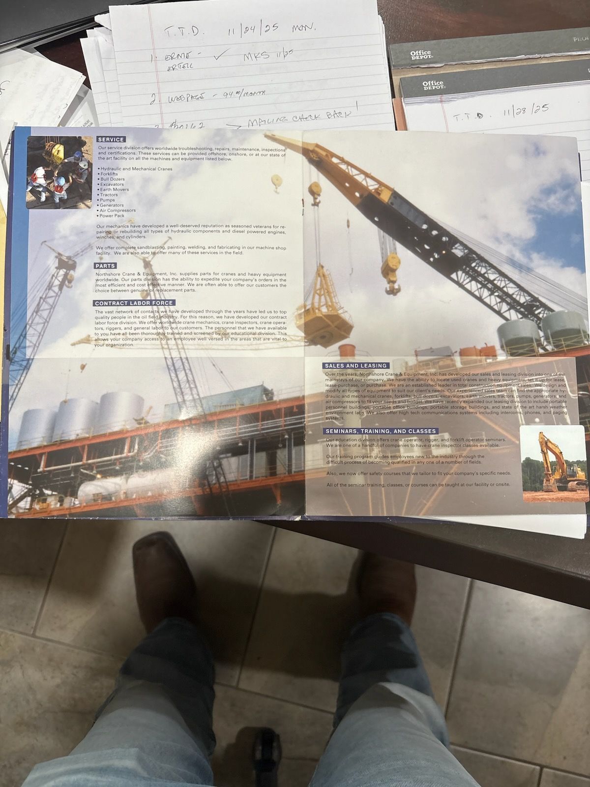 Open brochure displaying a crane lifting a load, set against a construction site with blue sky.