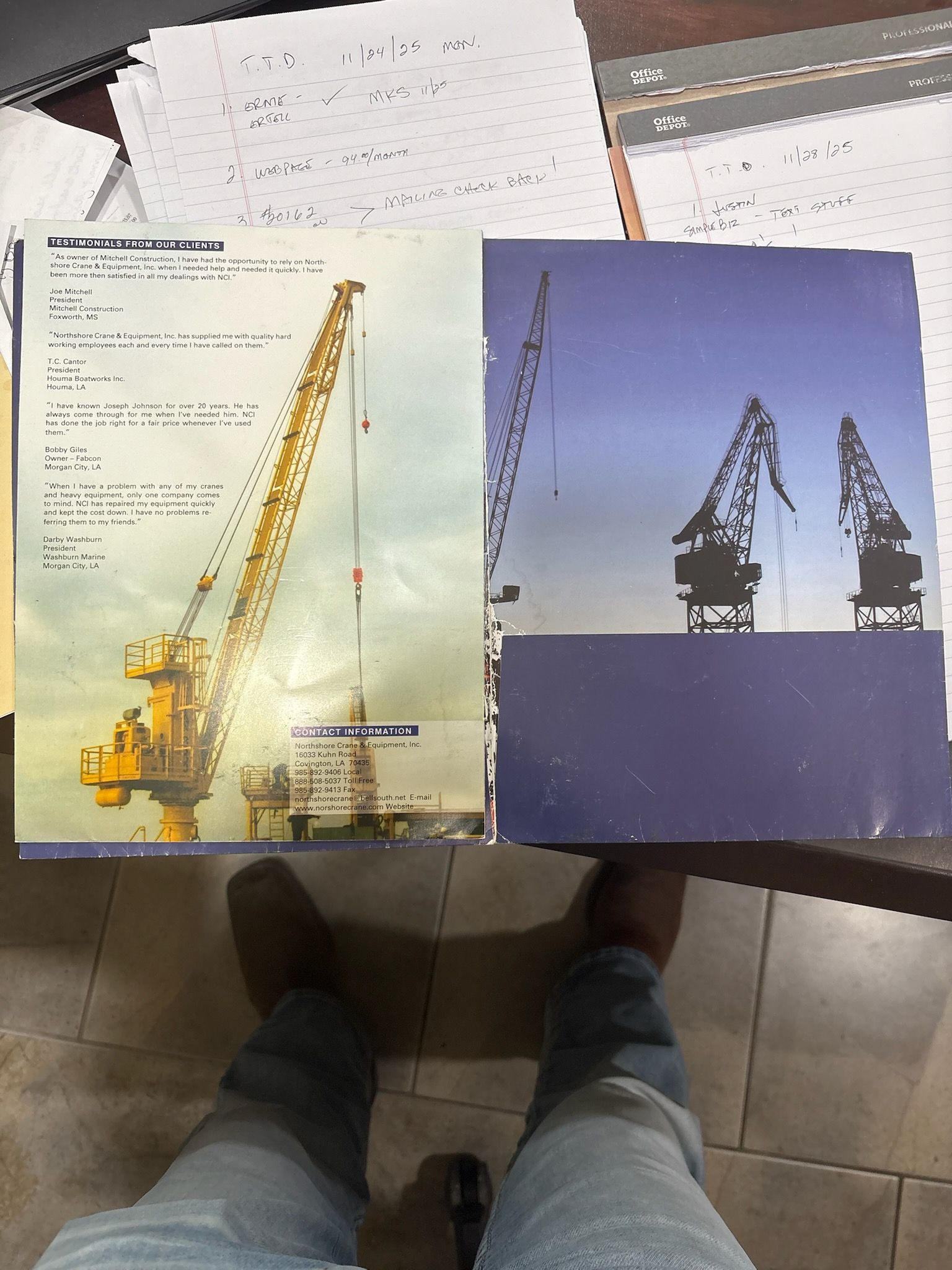 Open book showing industrial cranes, and a person's legs with jeans and brown shoes.
