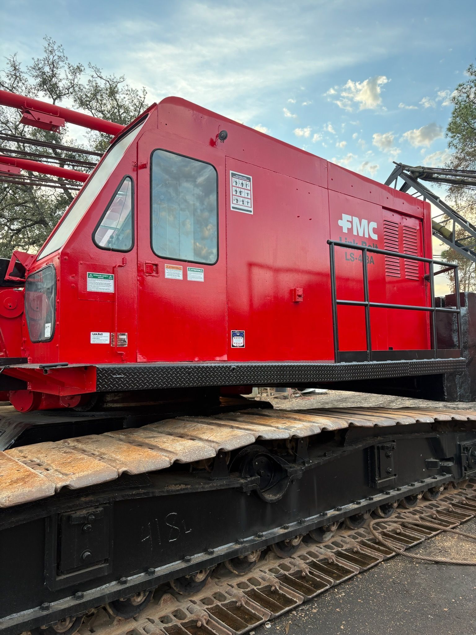 Red construction crane on a black track, with FMC logo, against a cloudy sky.