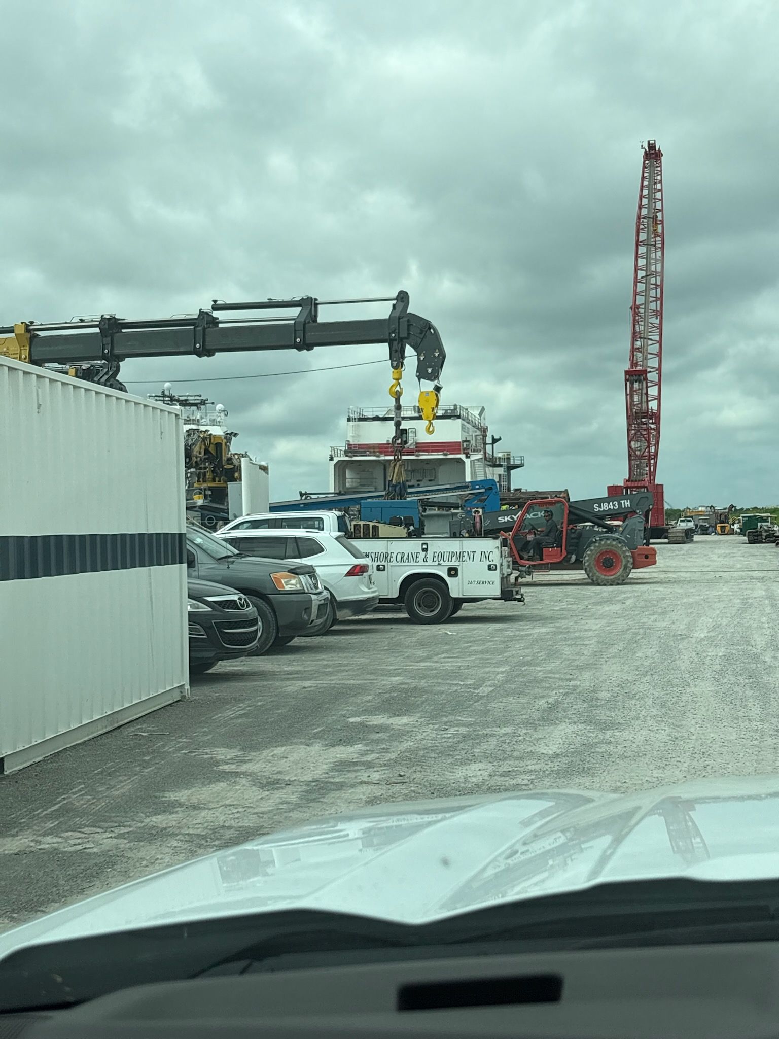 Oil rig site with crane, trucks, and equipment under cloudy sky.
