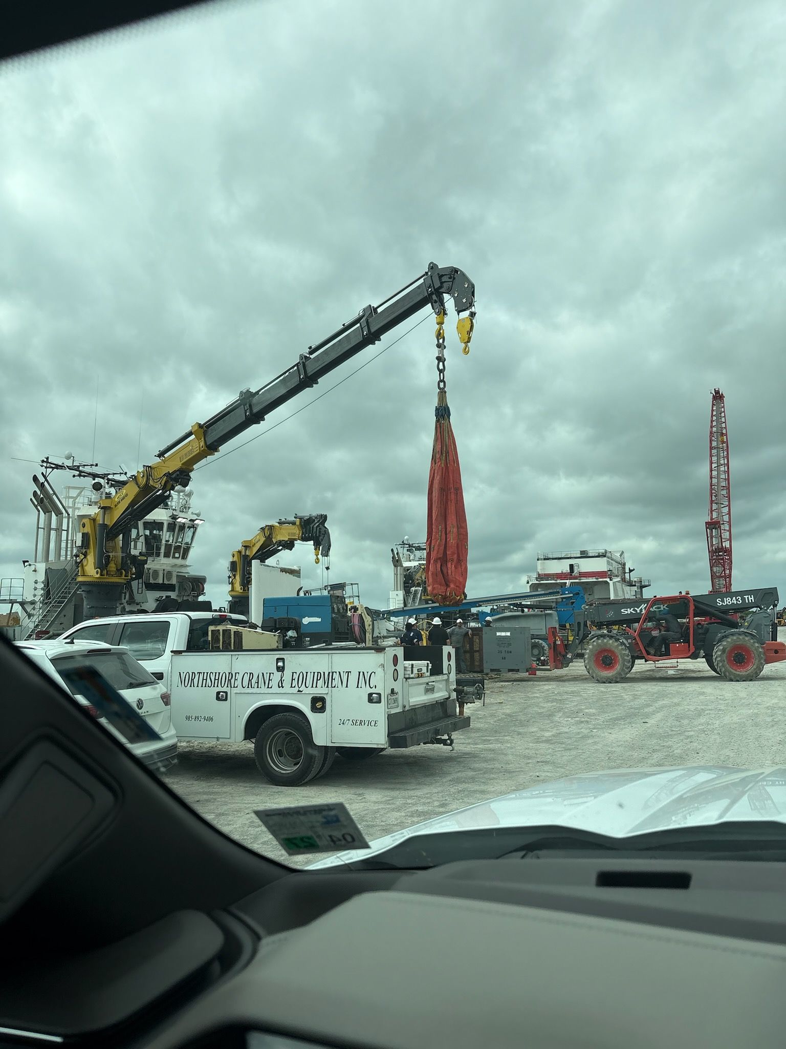 Oil rig operation with cranes and service trucks under cloudy skies.