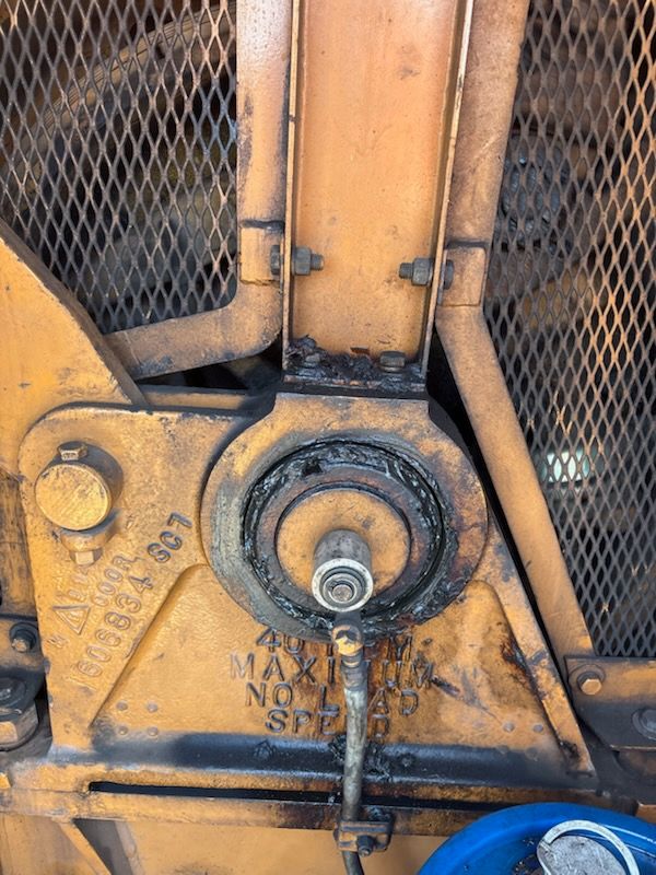 Close-up of industrial machinery, painted yellow, with a circular bearing and a visible grease fitting.