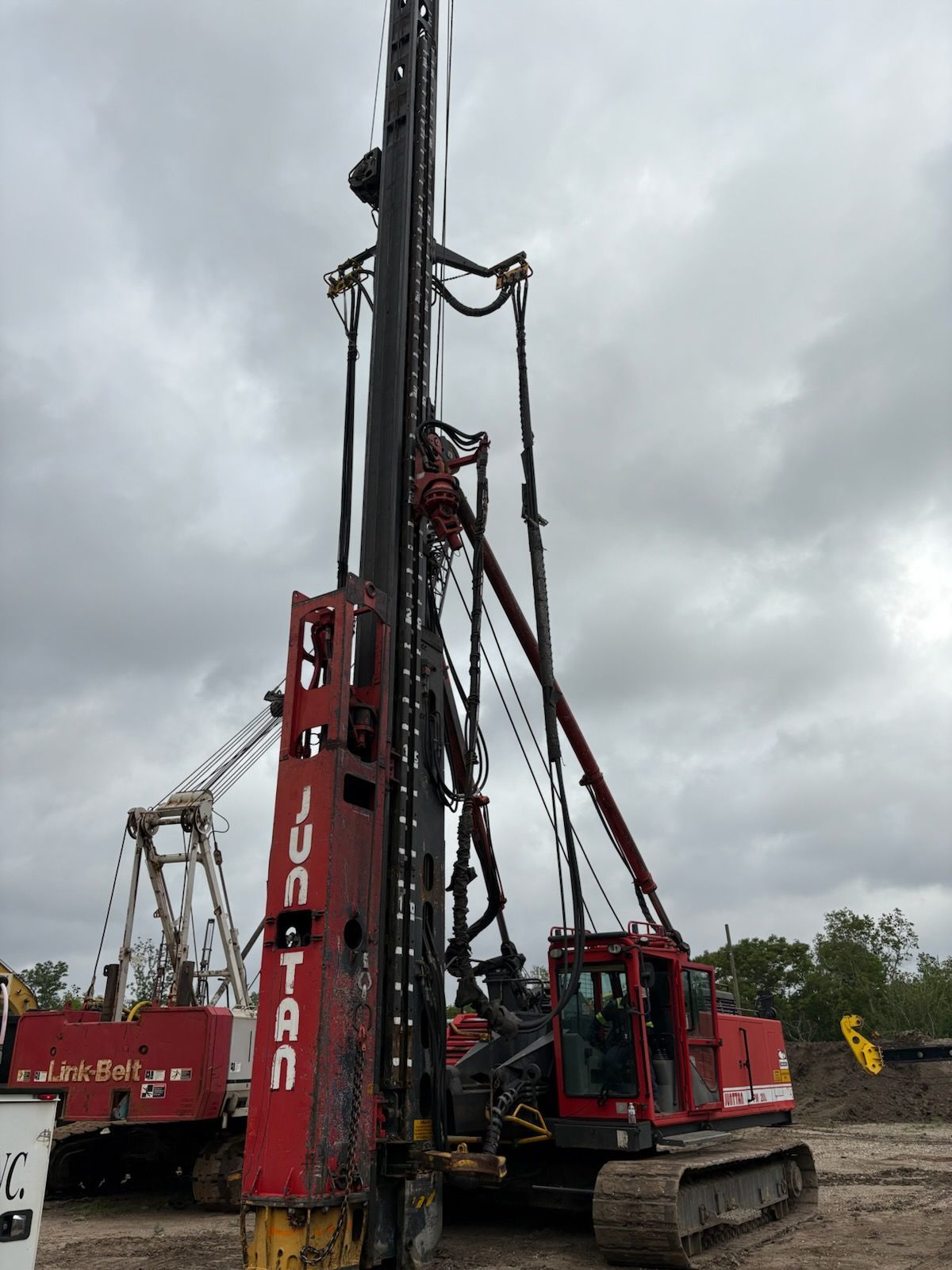 Red and black Junttan pile driving machine on a construction site under a cloudy sky.