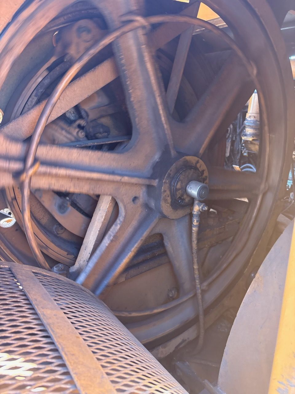Close-up of a large, rusty metal wheel with five spokes, inside an industrial machine.