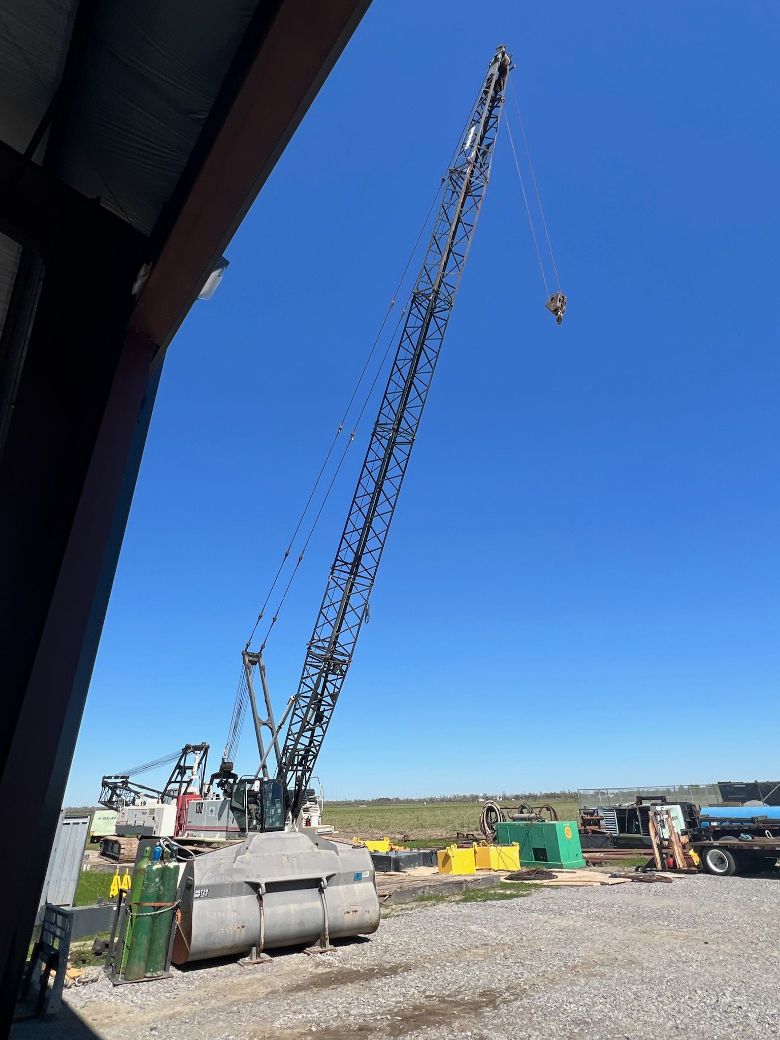 Crane lifting a heavy object against a clear blue sky. Construction site with support equipment visible.