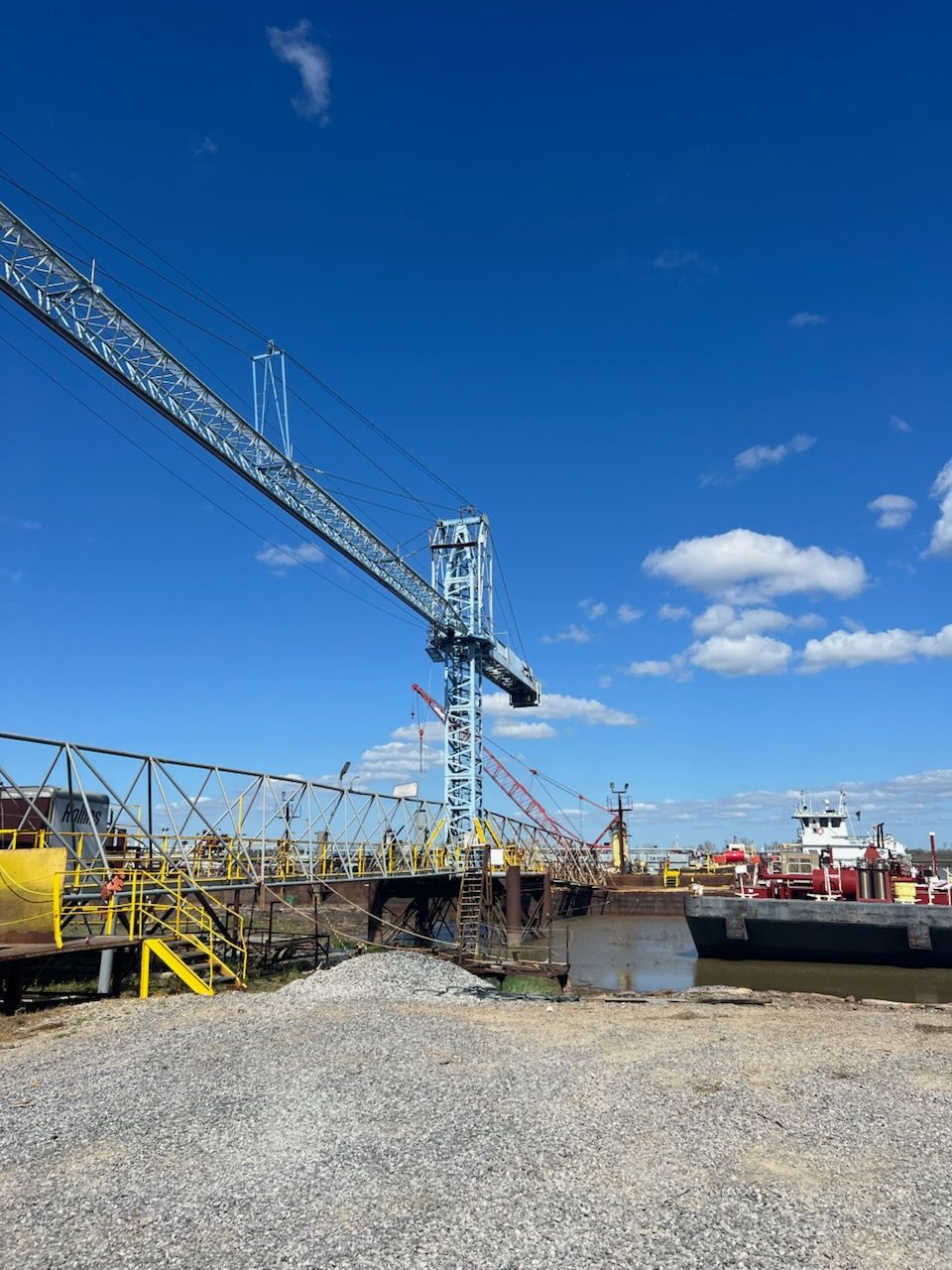Blue crane on a dock with a barge, under a partly cloudy blue sky.