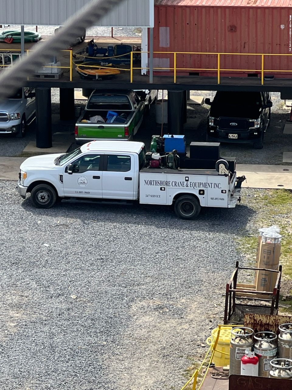 White work truck parked on gravel, with welding equipment visible. Other vehicles and a building in the background.