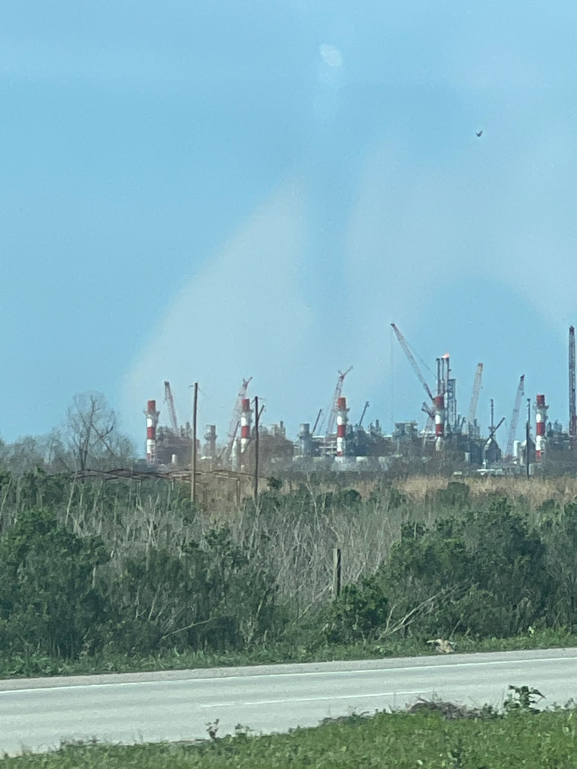 Oil refinery with numerous towers and cranes against a blue sky.