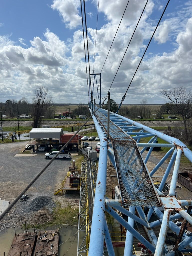 Blue crane arm with walkway, against cloudy sky, overlooking industrial site and landscape.
