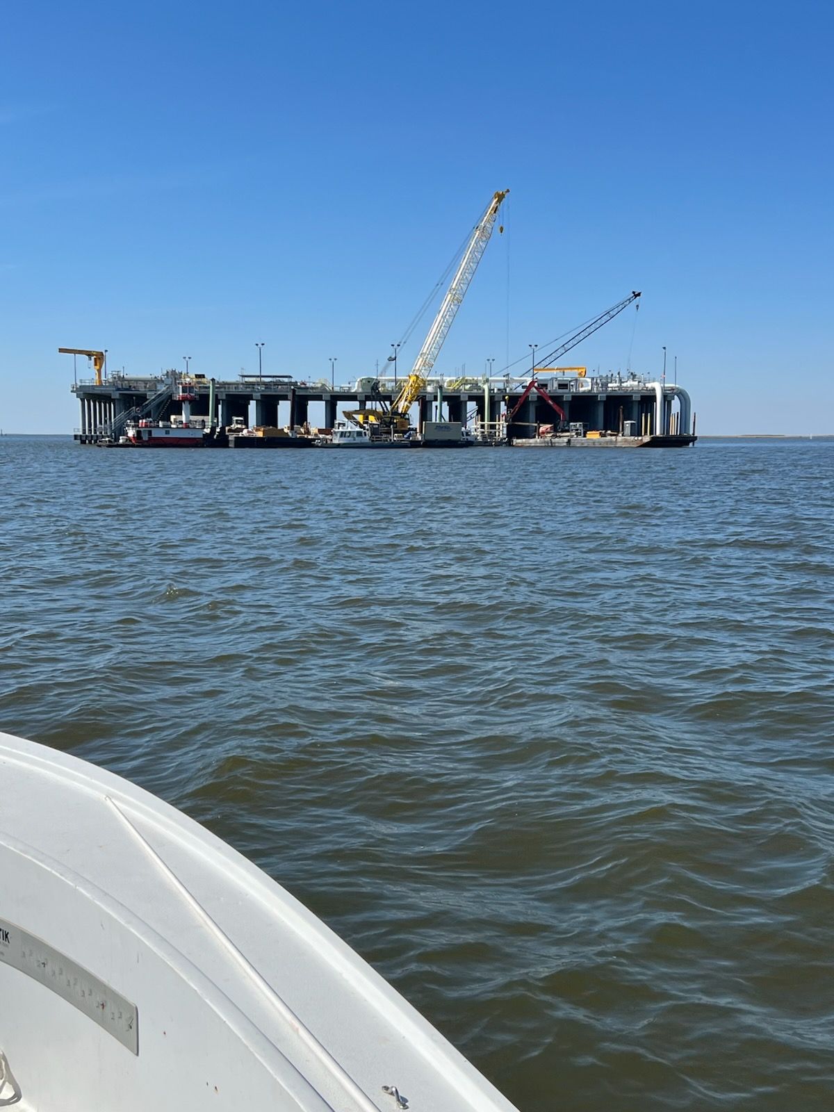 Large construction barge with cranes on water, under a blue sky.