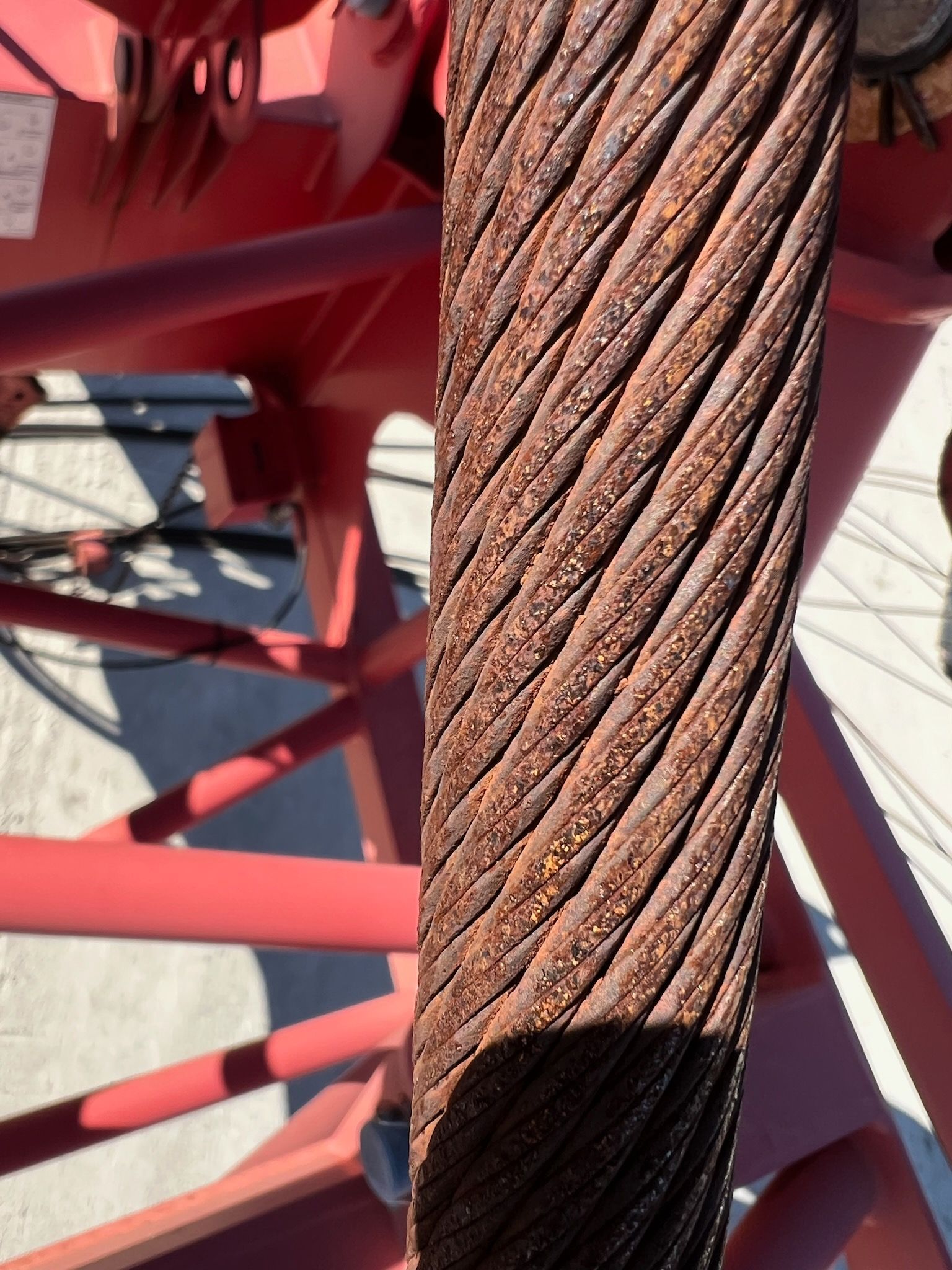 Close-up of a thick, rusty steel cable against a red support structure.