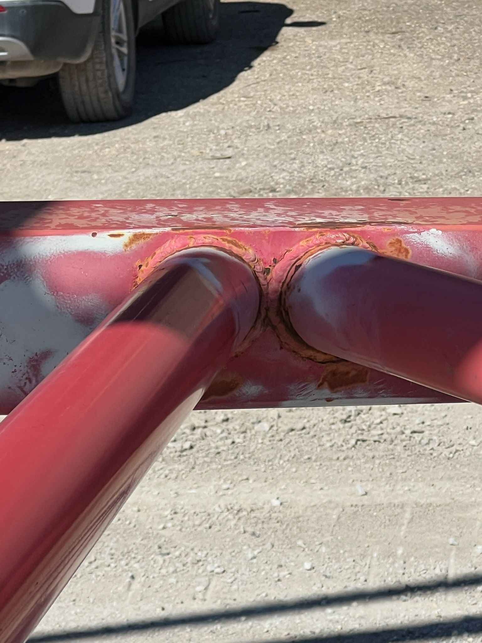 Red metal pipes welded together, showing rust. A vehicle tire is in the background.