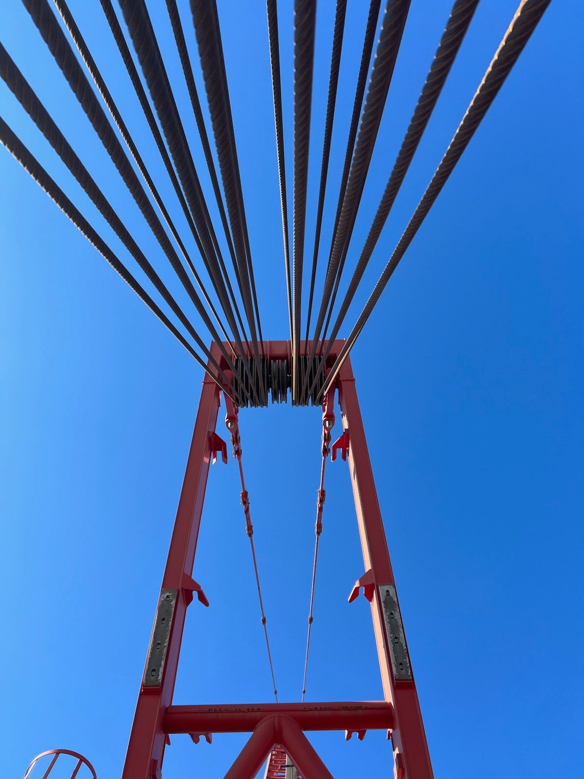 Red crane frame with many steel cables against a clear blue sky.