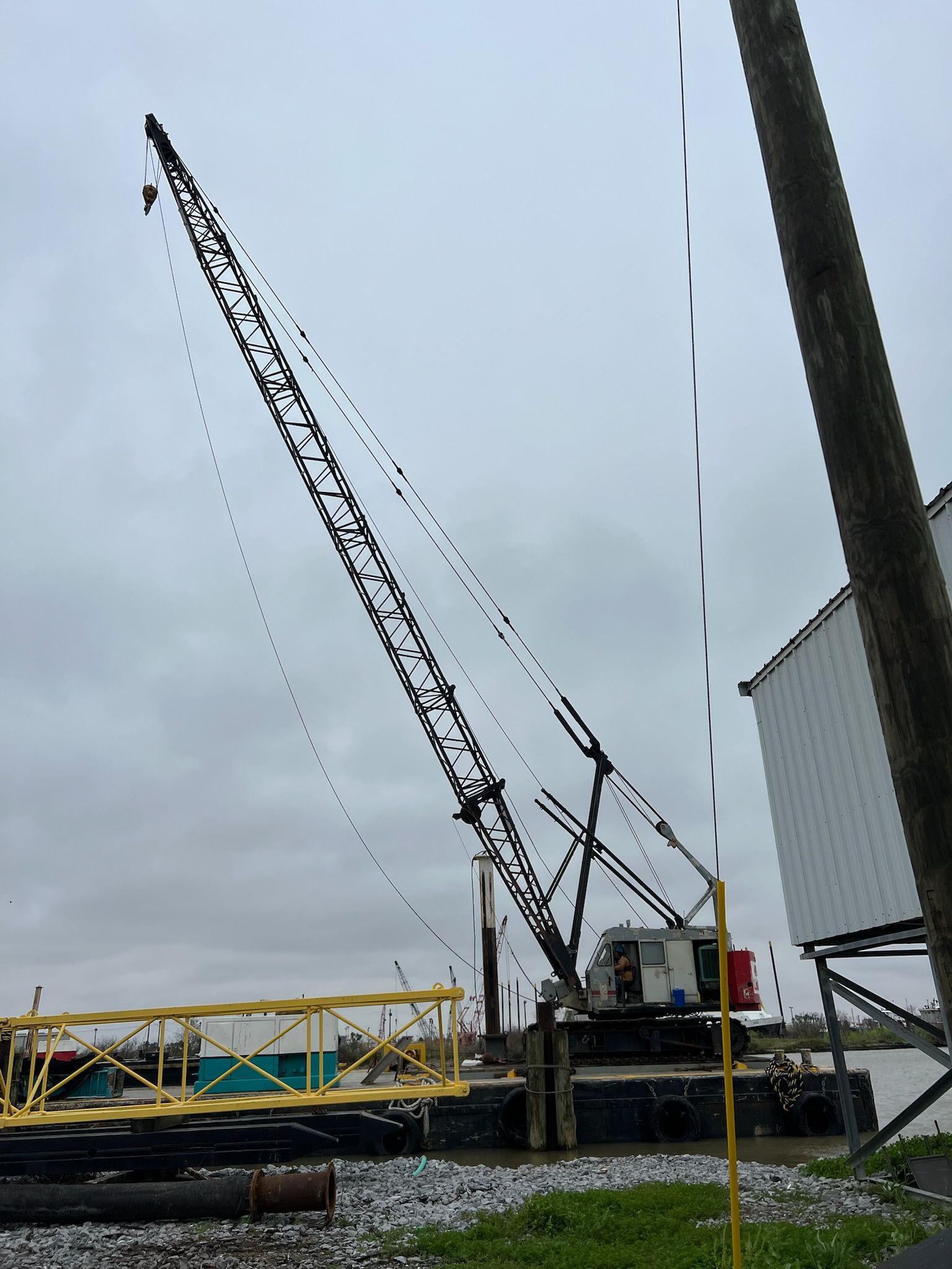 A large crane on a barge in murky water under an overcast sky. A yellow structure is attached to the barge.