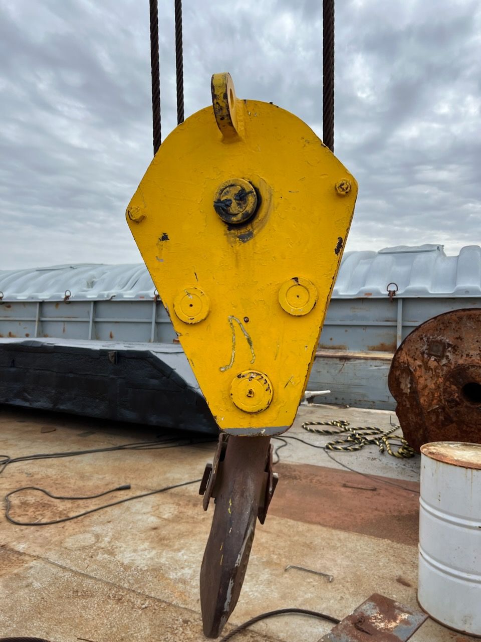 Yellow crane hook, with steel cable, hanging in industrial setting.