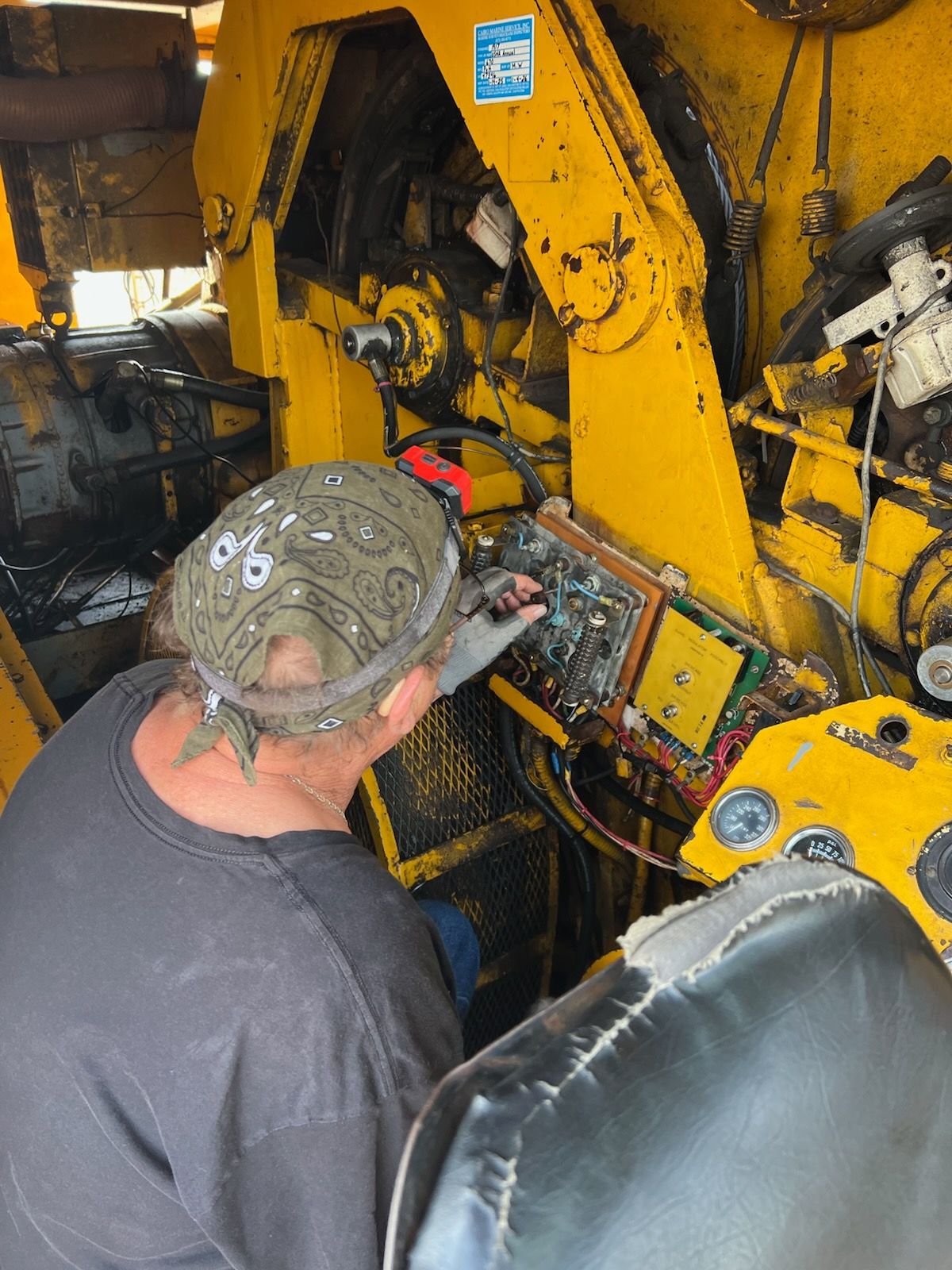Man working on machinery, inspecting a circuit board. Yellow machine interior, grimy setting.