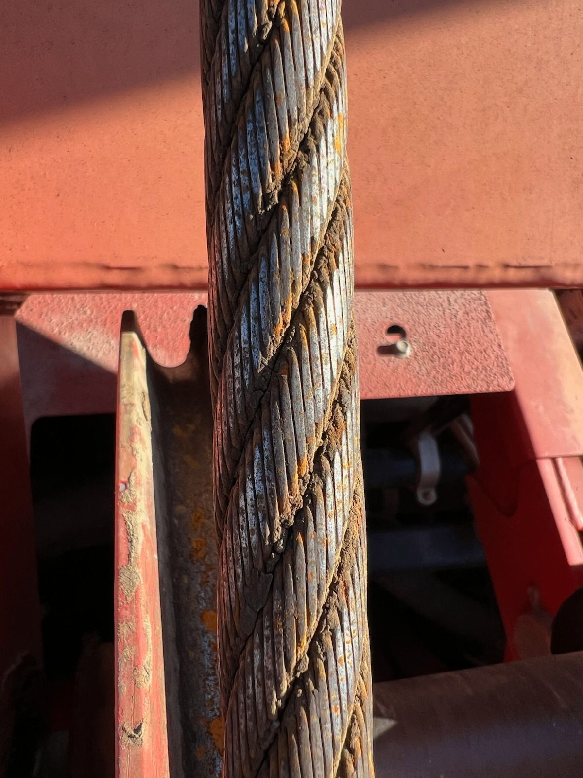 Rusty steel cable, close-up. Shows twisted strands with rust, against red equipment.