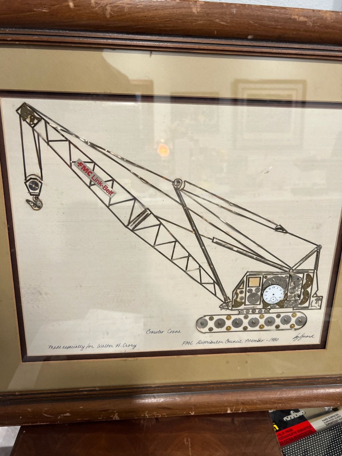 Drawing of a crane in a frame, with brown wood border. Crane has red lettering.