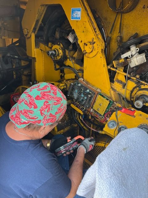 Person in a lobster print cap works on yellow machinery with tools.