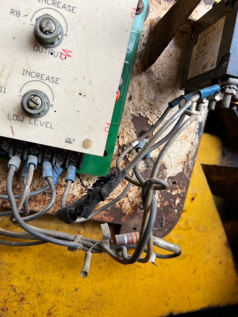 Close-up of industrial electrical components with wires, showing damage and wear on a rusty yellow surface.