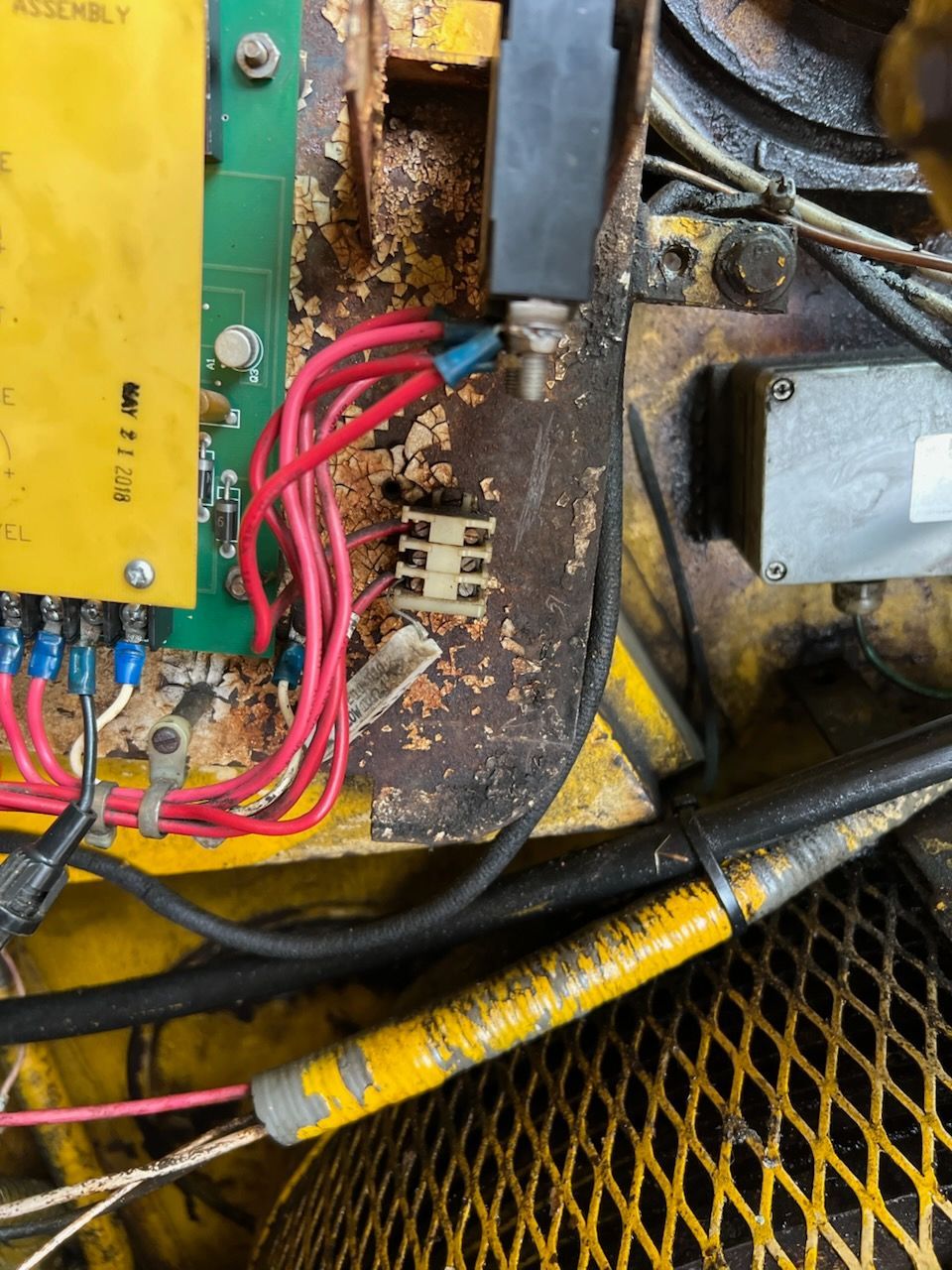 Close-up of electrical components with red and blue wires, mounted on a yellow metal surface, with a black wire bundle.