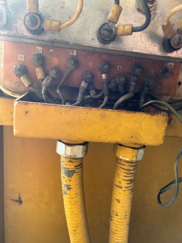 Yellow electrical junction box with wires and conduit, bolted to a panel.