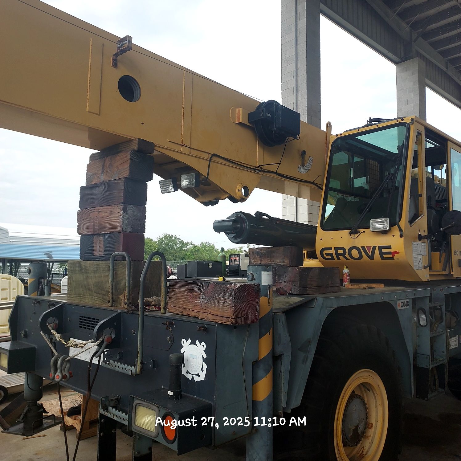 Yellow Grove crane with its boom resting on stacked bricks, parked outdoors under a partial shelter.