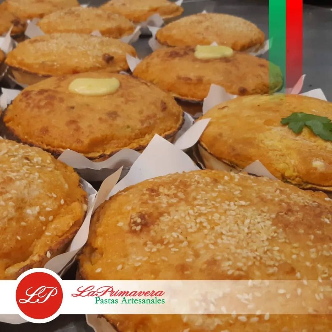 Primer plano de empanadas horneadas con semillas de sésamo, envoltorios de papel y un logotipo.