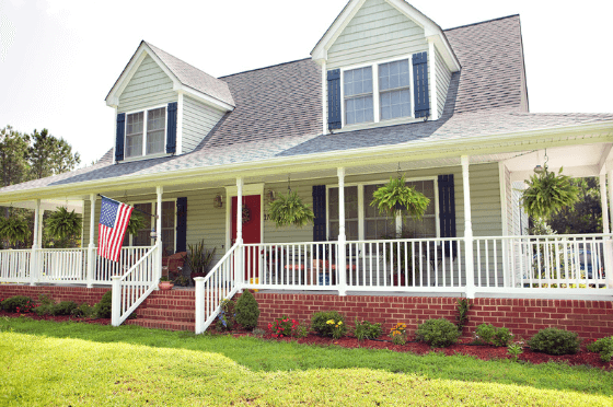 exterior home painted sage green with a white porch and red door shown during the day