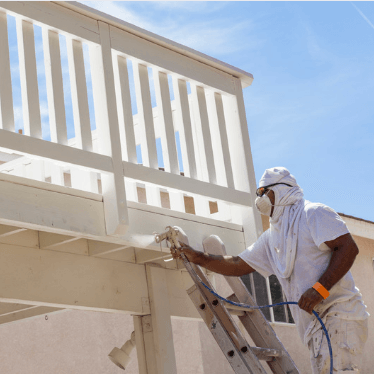 professional painting contractor spraying cream paint on fence and decking