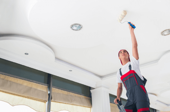 professional painting contractor up on a ladder rolling a ceiling with white paint
