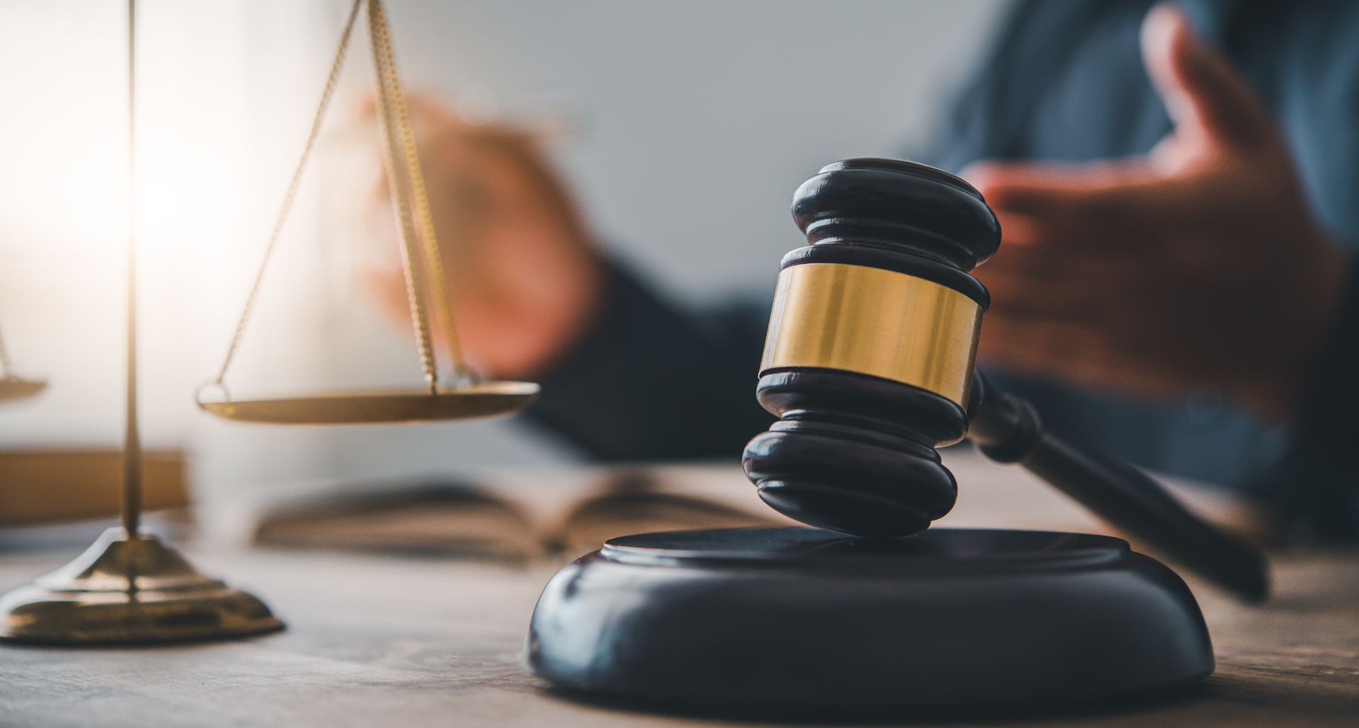 A judge is holding a gavel in front of a scale of justice.