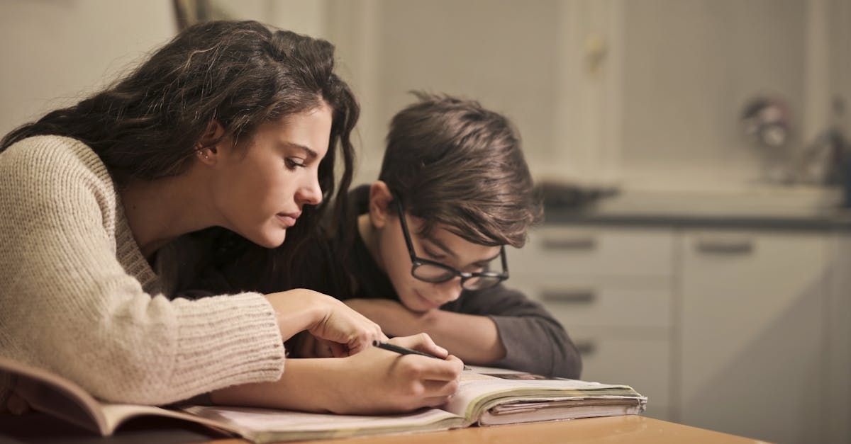A woman is helping a boy with his homework at a table.