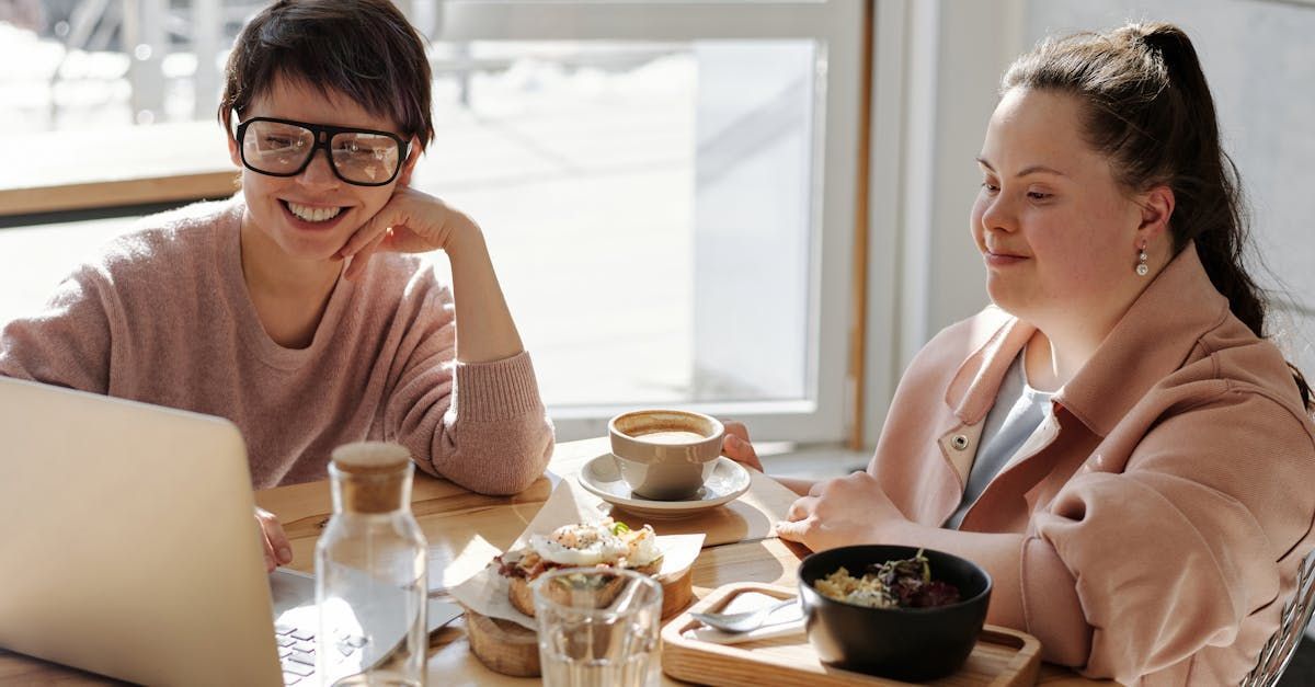 Two women are sitting at a table looking at a laptop.