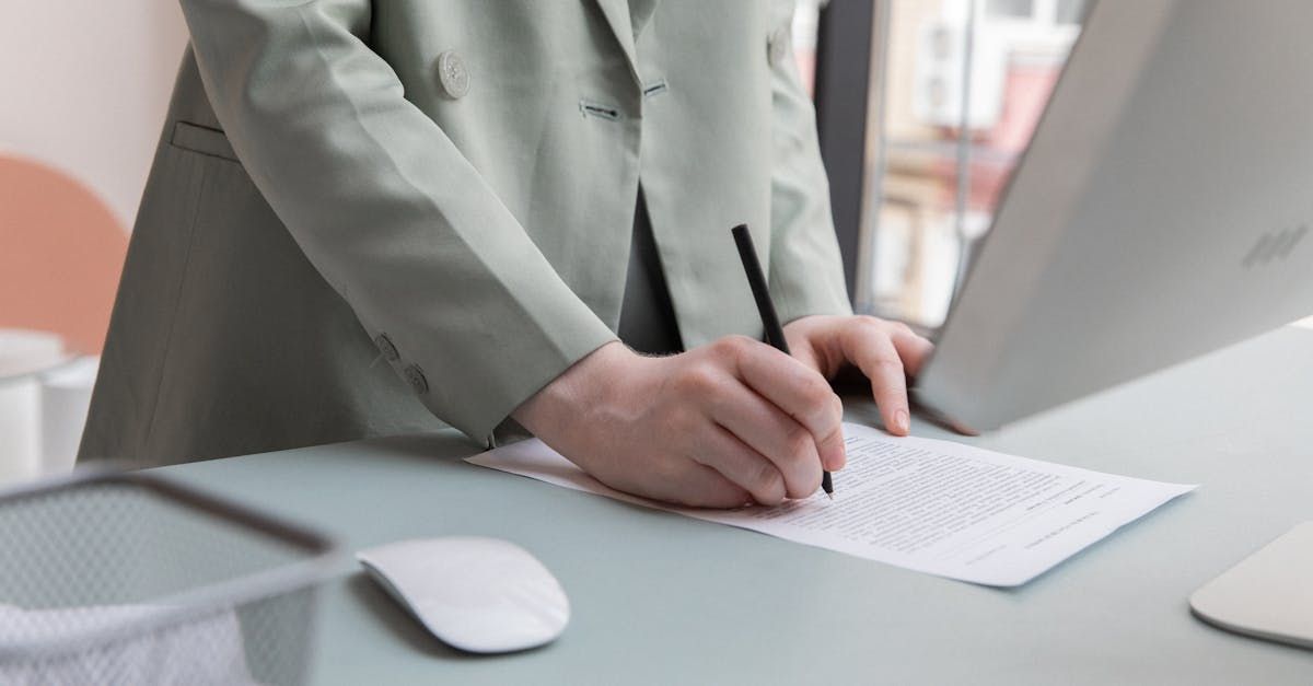 A person is writing on a piece of paper while using a laptop computer.