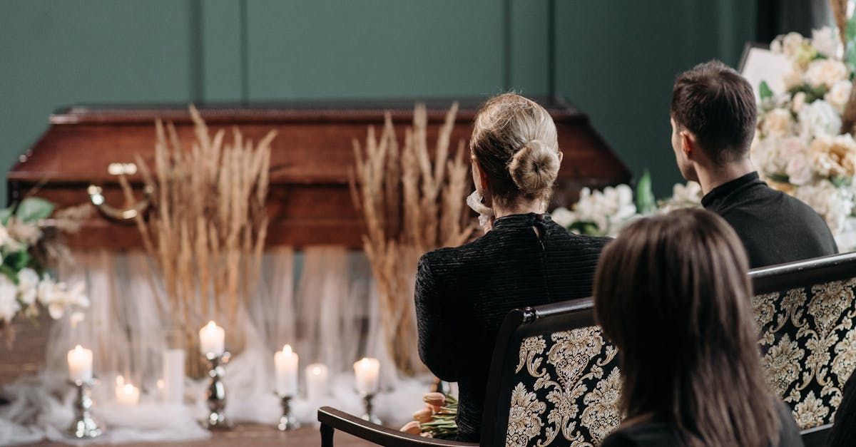 A man and a woman are sitting in front of a coffin at a funeral.