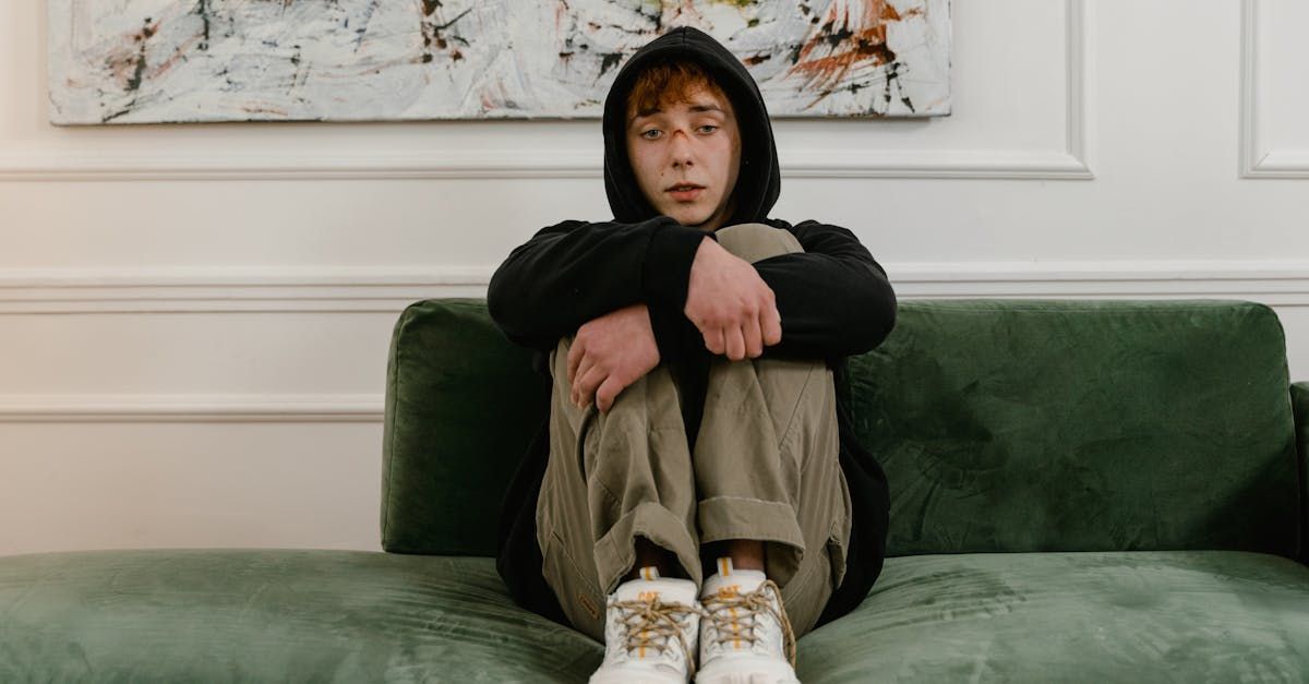 A young man is sitting on a green couch with his legs crossed.