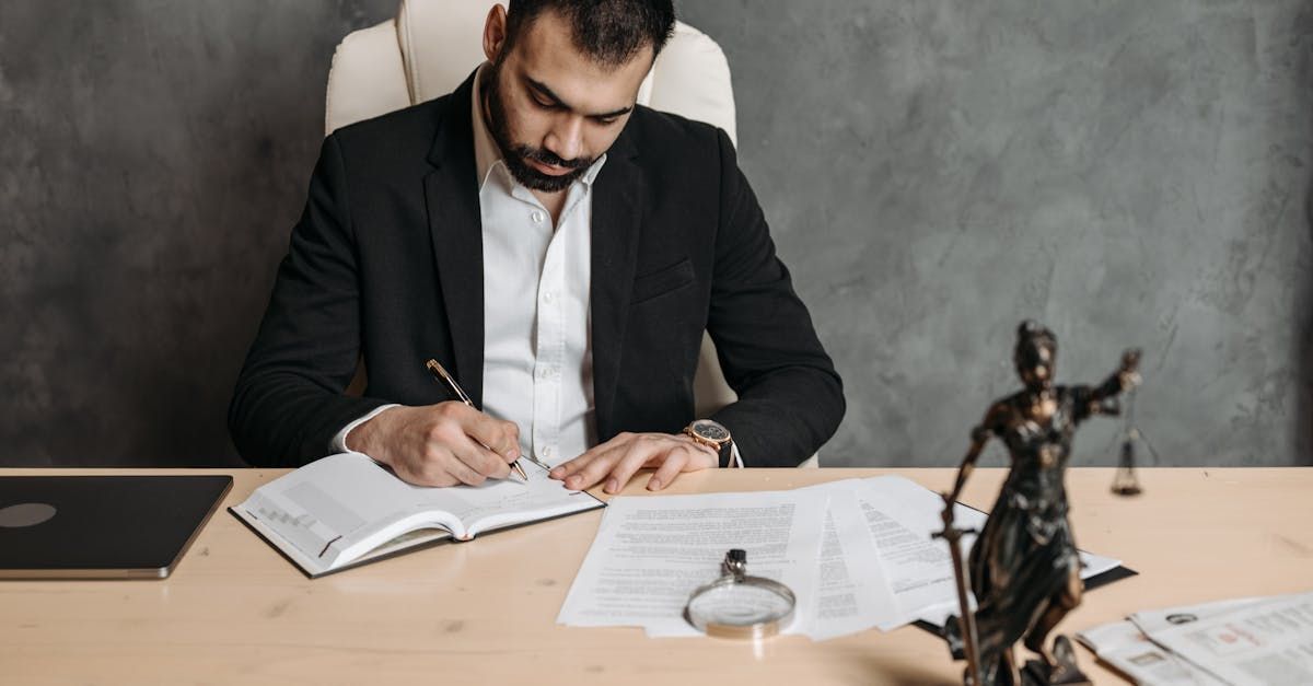 A man in a suit is sitting at a desk writing in a notebook.
