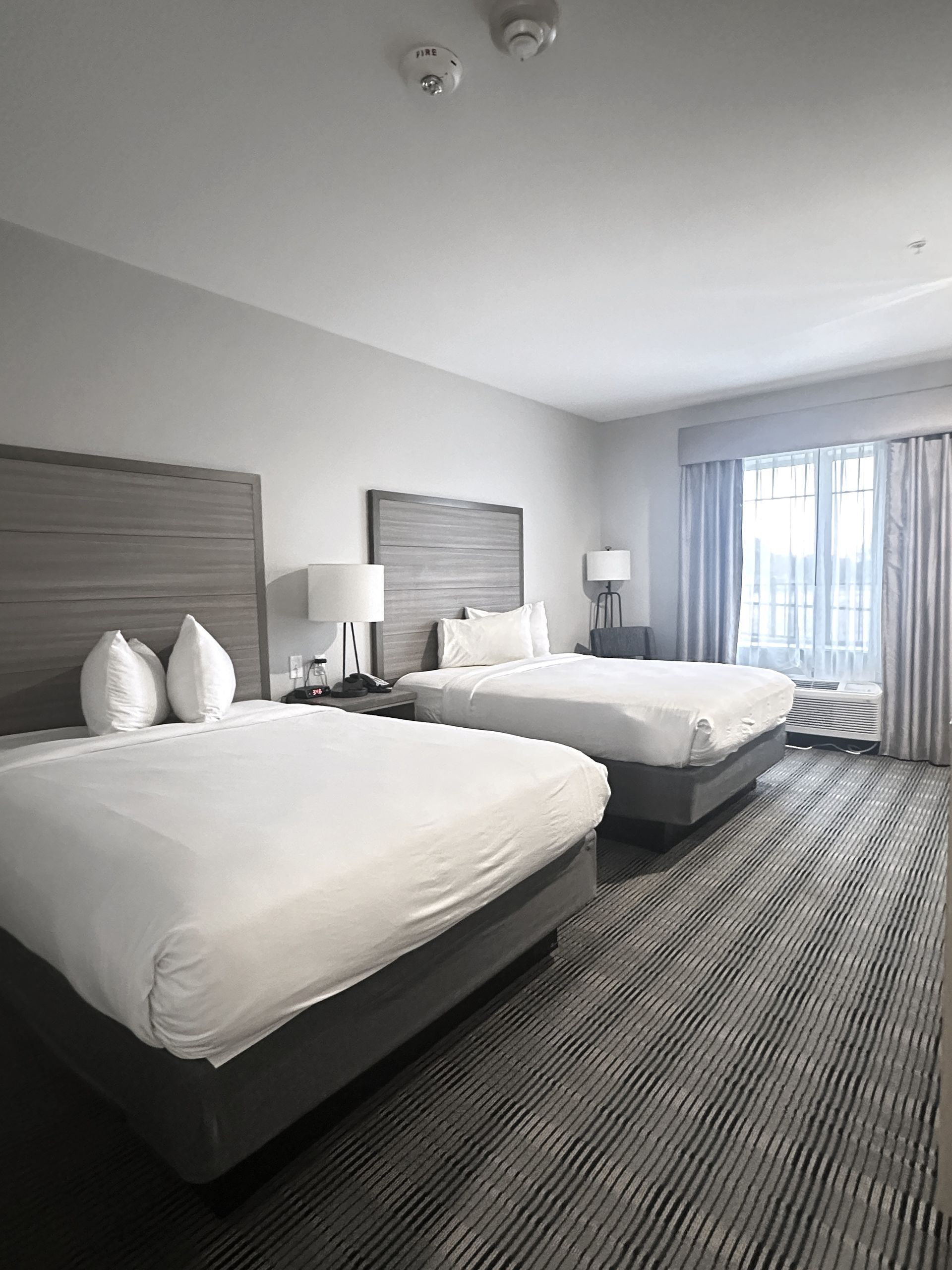 Two double beds in a hotel room with light grey headboards, white bedding, and a striped rug.