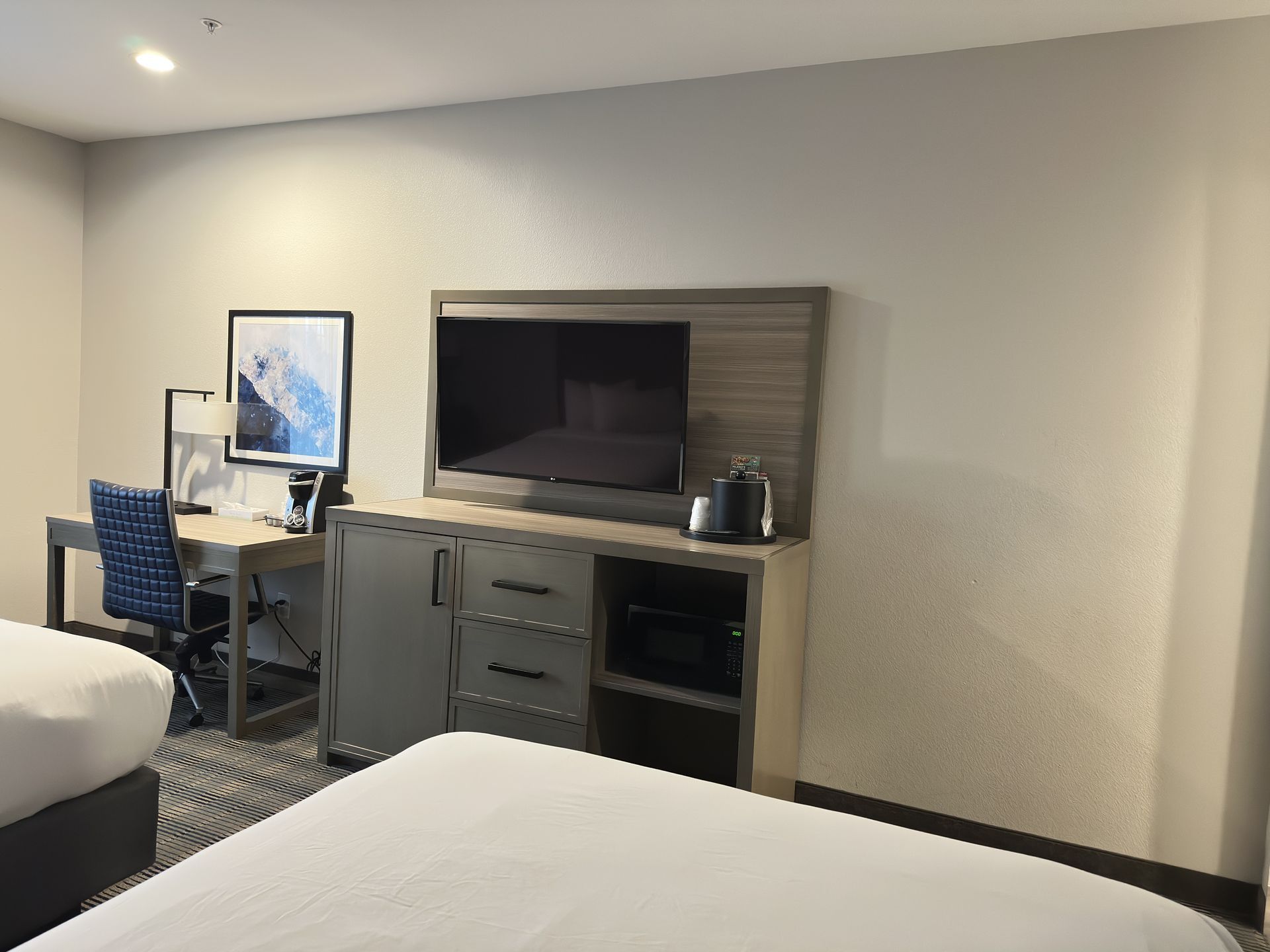 Hotel room with two beds, desk with chair, TV on cabinet, and artwork.