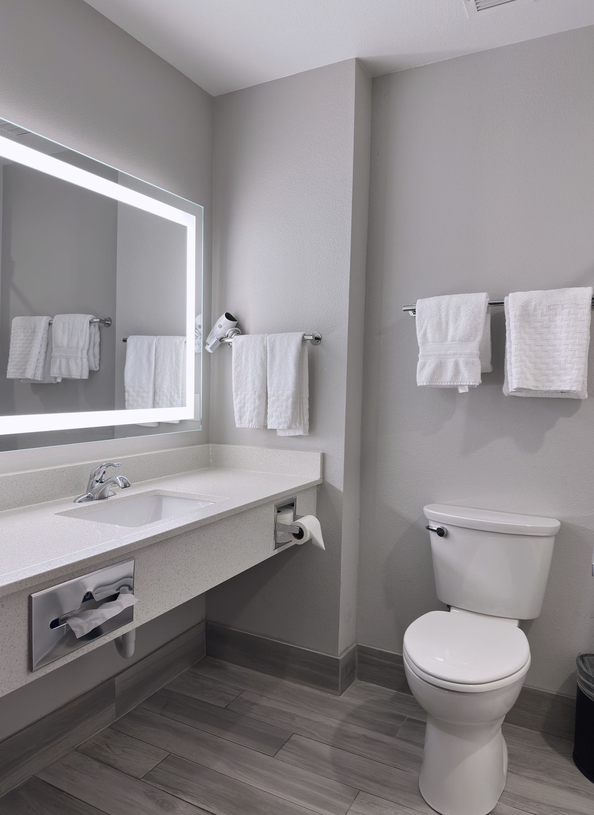 Bathroom with a white toilet, vanity, and towels; gray walls and flooring.