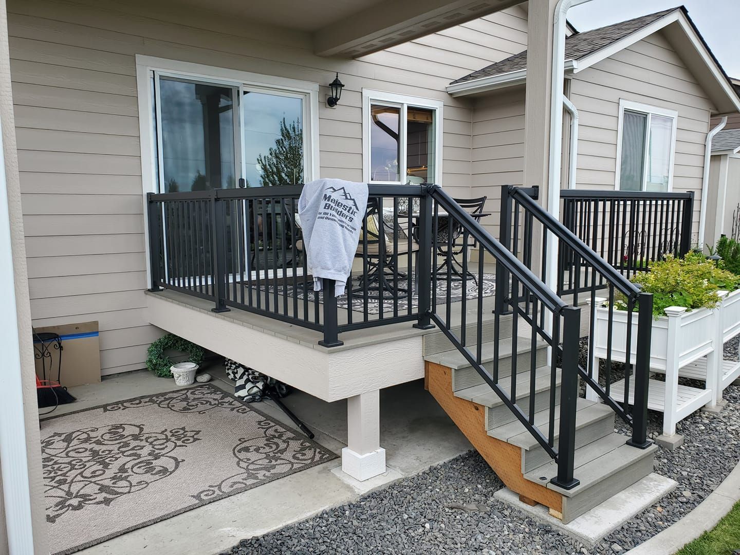 Front porch with black railings and stairs, white siding, and a hanging sign beside the entrance.